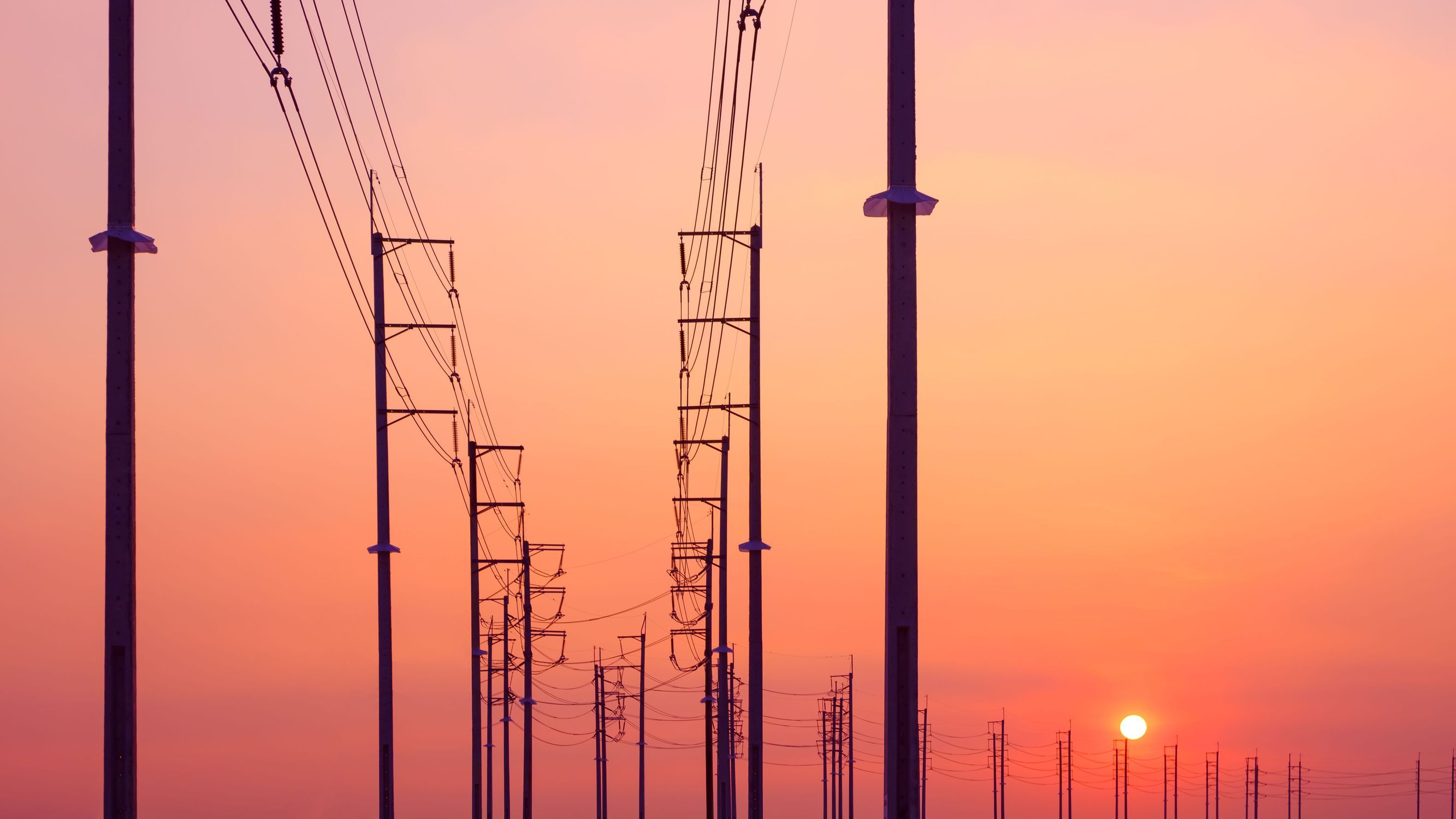 Overhead power lines curve in front of a glowing sunset